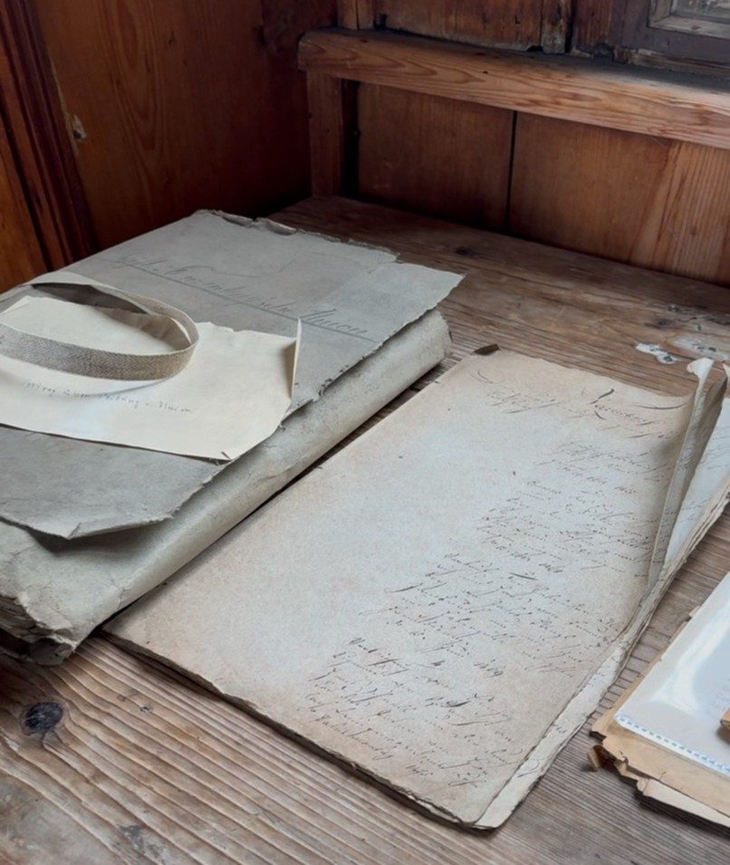 Historische Aktenumschläge und Schriftstücke auf einem Holztisch auf dem Dachboden